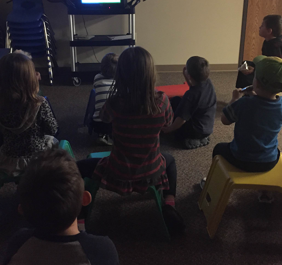The class sits in their detachable stools and watches Dora the Explorer